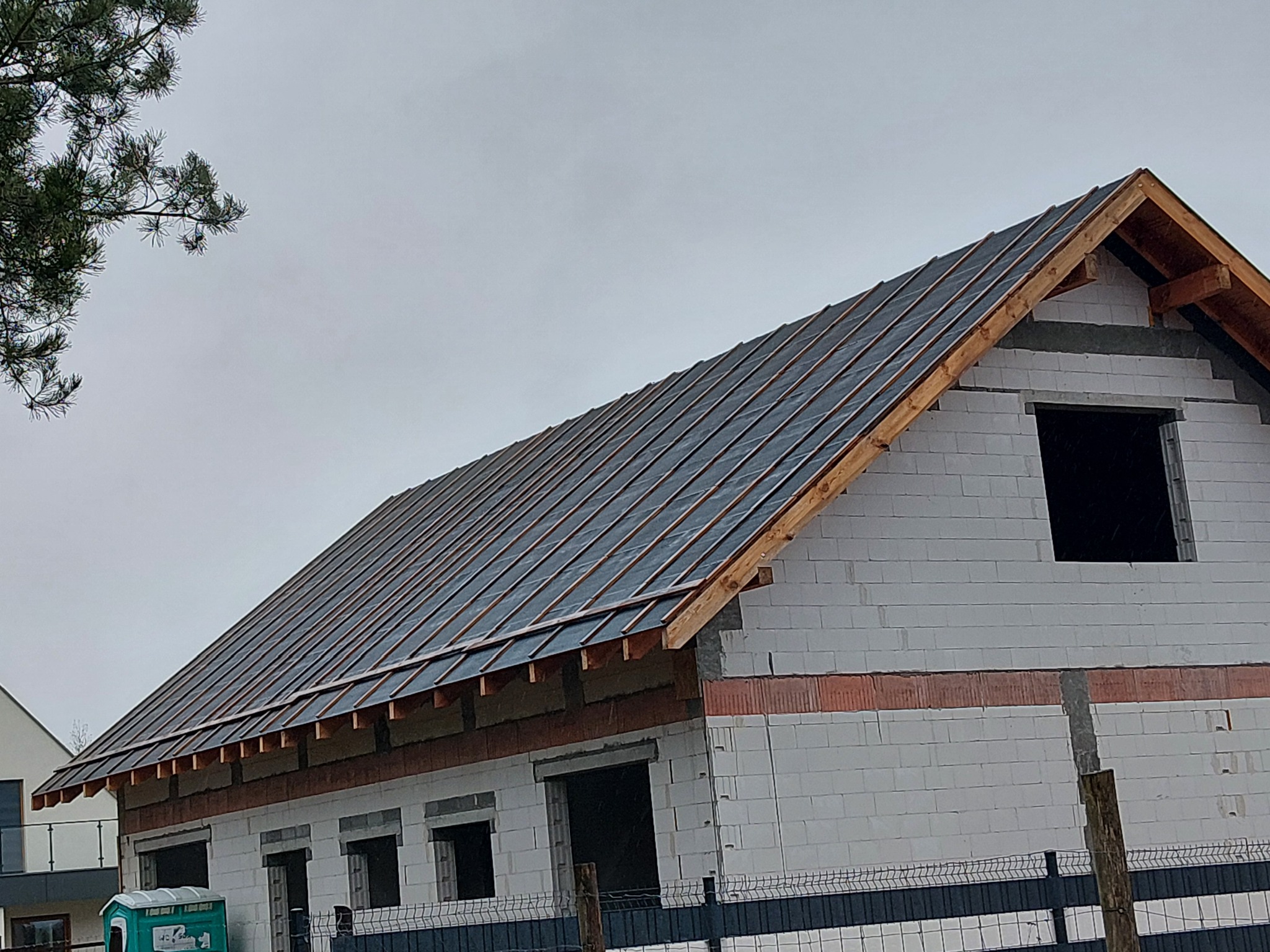 Budowa dachu domu jednorodzinnego w trakcie realizacji. Widoczna więźba i wstępne krycie folią. Ściany z białego bloczka.