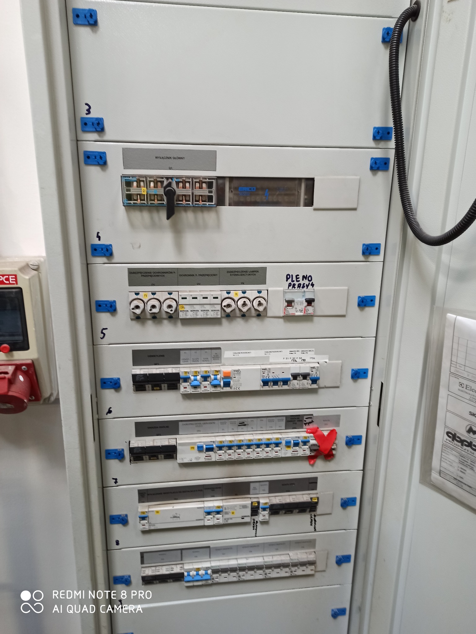 Rozdzielnica elektryczna z wyłącznikami, bezpiecznikami i oznaczeniami, widok z bliska na zamontowane zabezpieczenia i komponenty elektryczne.