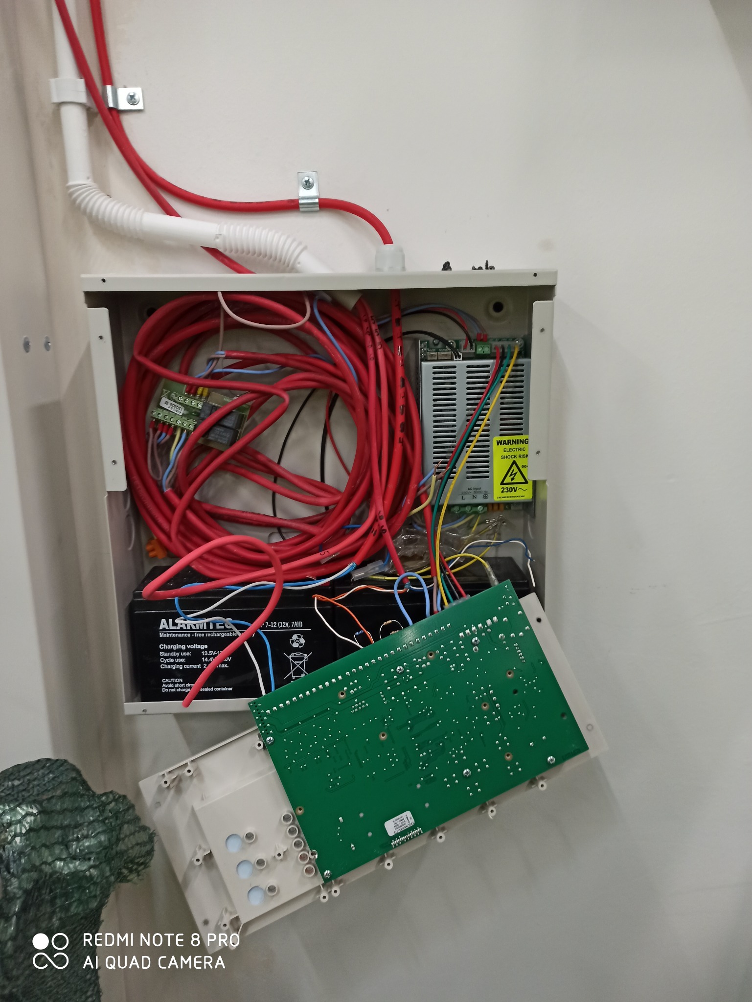 Otwarta skrzynka z okablowaniem alarmowym, akumulatorem i płytką drukowaną we Wrocławiu. Czerwone kable i elementy elektryczne wewnątrz obudowy.