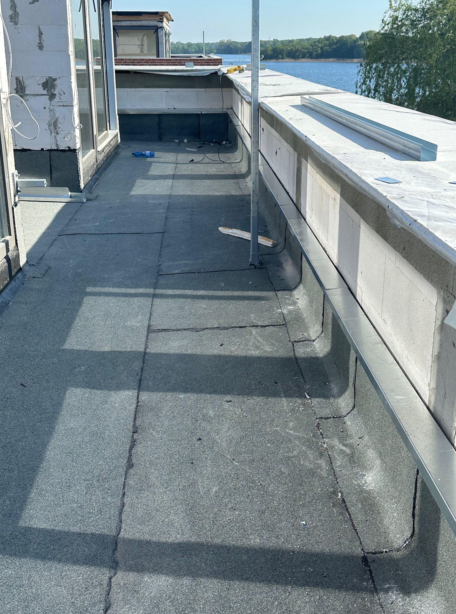 Wykończony dach płaski z papy termozgrzewalnej, obróbki blacharskie, widok na rzekę w tle. Detal wykonania dachu, hydroizolacja, zabezpieczenie przed wodą.