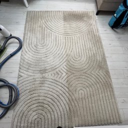 Fresh Space - Dywan z geometrycznym wzorem, częściowo wyczyszczony, z widocznym odkurzaczem piorącym i fragmentem podłogi. Widoczne różnice w kolorze włókien.