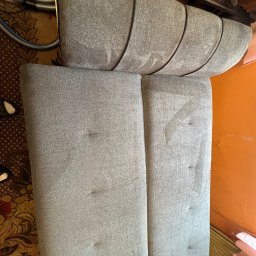 Fresh Space - Szara kanapa z widocznymi śladami czyszczenia, fragment węża odkurzacza w tle. Widoczne różnice w odcieniu po praniu tapicerki.