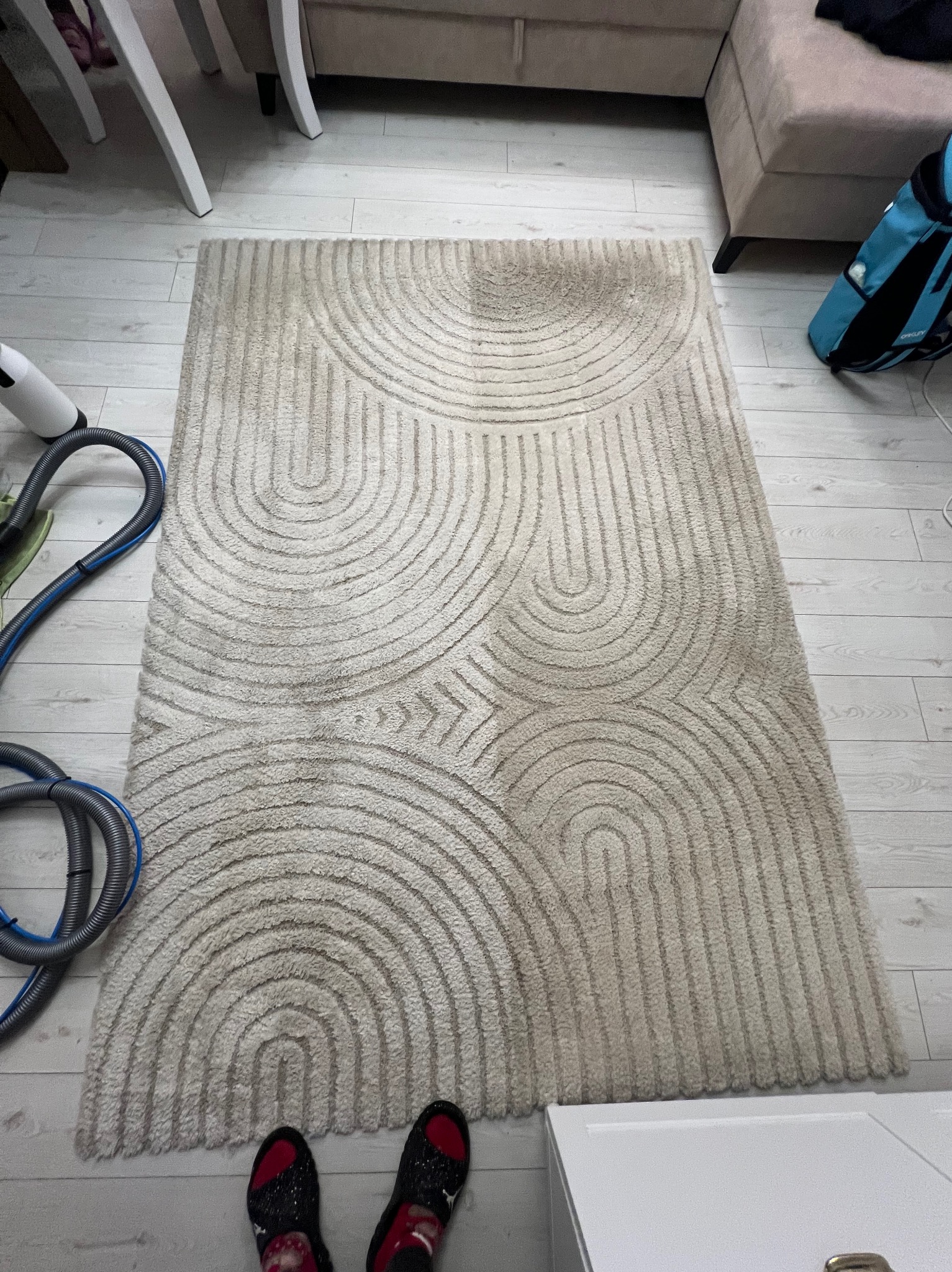 Dywan z geometrycznym wzorem, częściowo wyczyszczony, z widocznym odkurzaczem piorącym i fragmentem podłogi. Widoczne różnice w kolorze włókien.