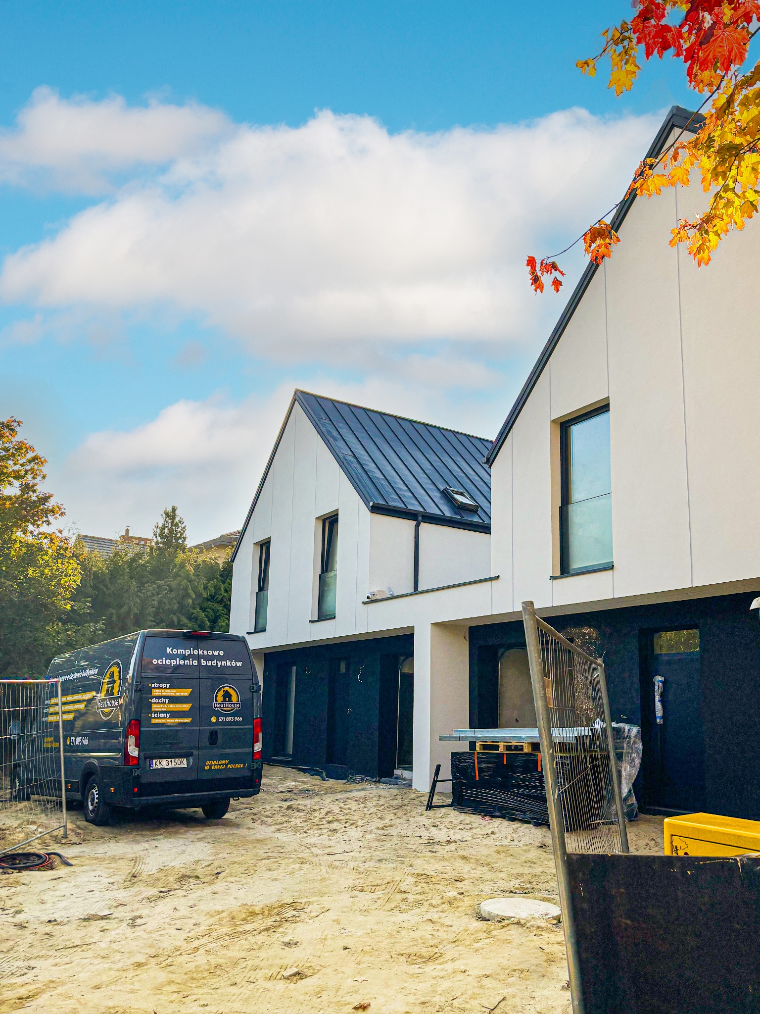 Nowoczesny dom po kompleksowym ociepleniu w Warszawie, z widocznym autem firmy HeatHouse. Elewacja biała, dach ciemny, jesienne liście w rogu kadru.