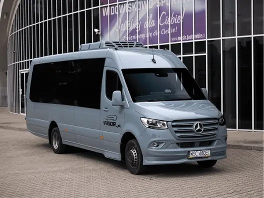Szary bus Mercedes-Benz Sprinter z klimatyzacją na dachu, zaparkowany przed budynkiem z dużymi oknami. Widoczne logo firmy FIGOR.pl i tablica rejestracyjna.