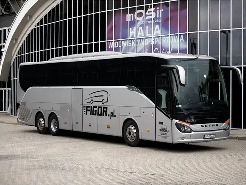Srebrny autokar Setra z otwartymi drzwiami na tle nowoczesnego budynku MOSiR. Logo firmy przewozowej FIGOR.pl widoczne na boku pojazdu.