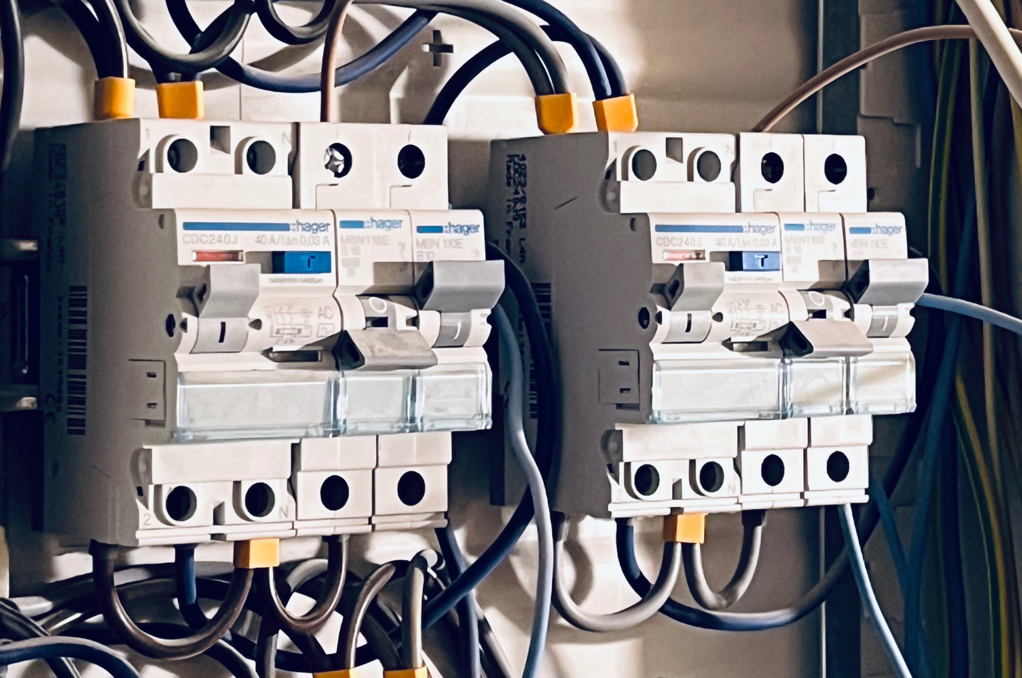 Dwa białe wyłączniki Hager z podłączonymi przewodami w różnych kolorach, zamontowane w skrzynce elektrycznej. Widoczne oznaczenia i parametry urządzeń.