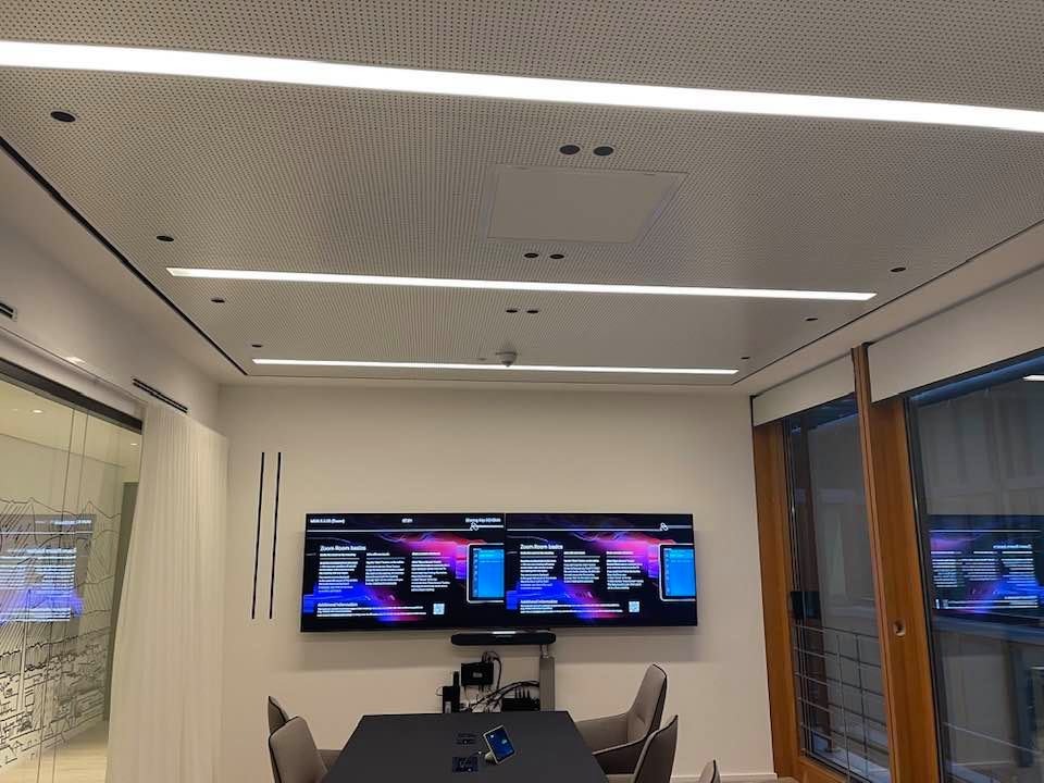 Nowoczesna sala konferencyjna z podwieszanym sufitem z oświetleniem liniowym LED. Dwa ekrany na ścianie. Widok na salę przez szklaną ścianę.