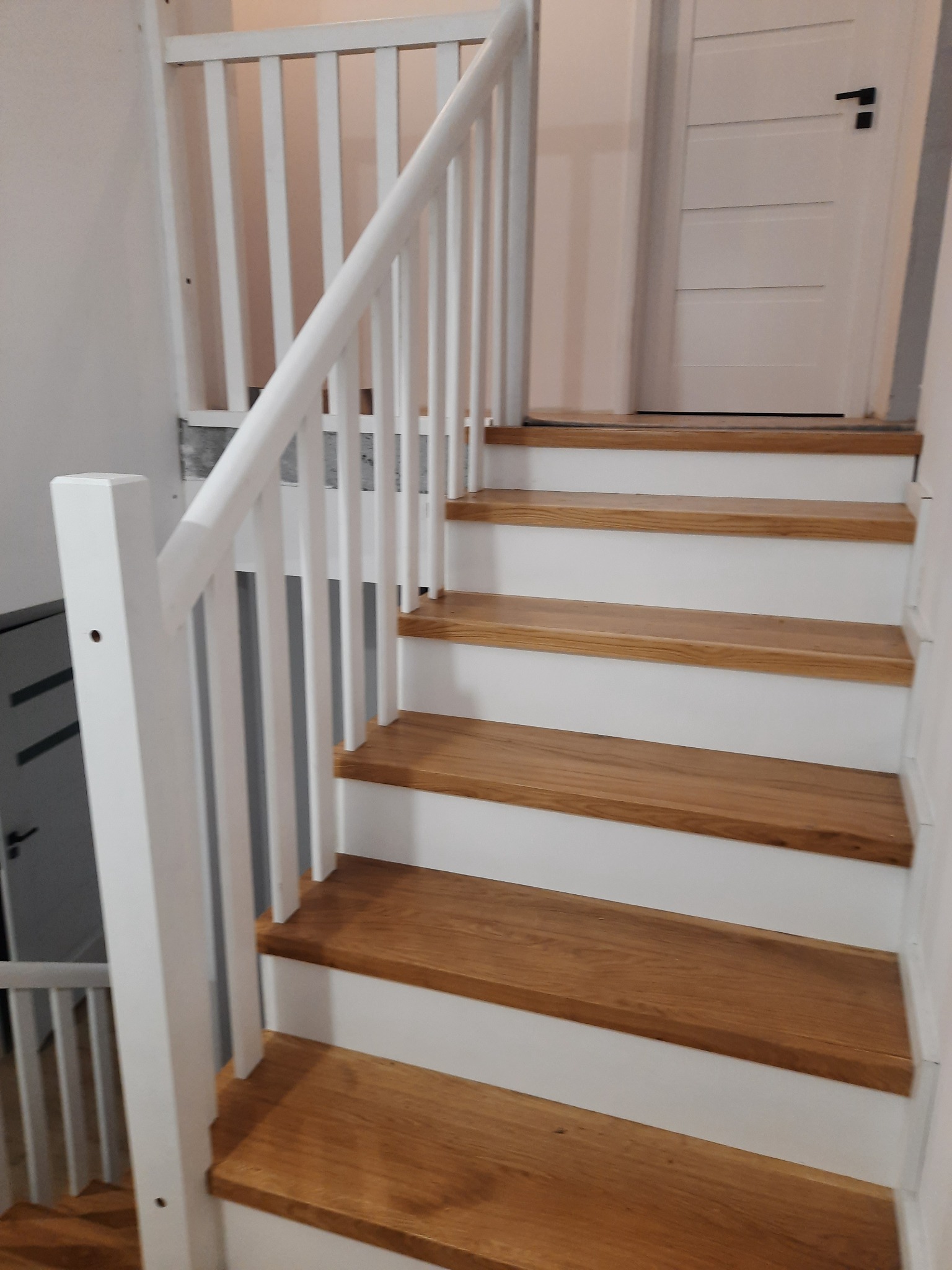Jasne, drewniane stopnie schodów z białą balustradą w nowoczesnym domu. Widoczne detale wykończenia i minimalistyczny design.