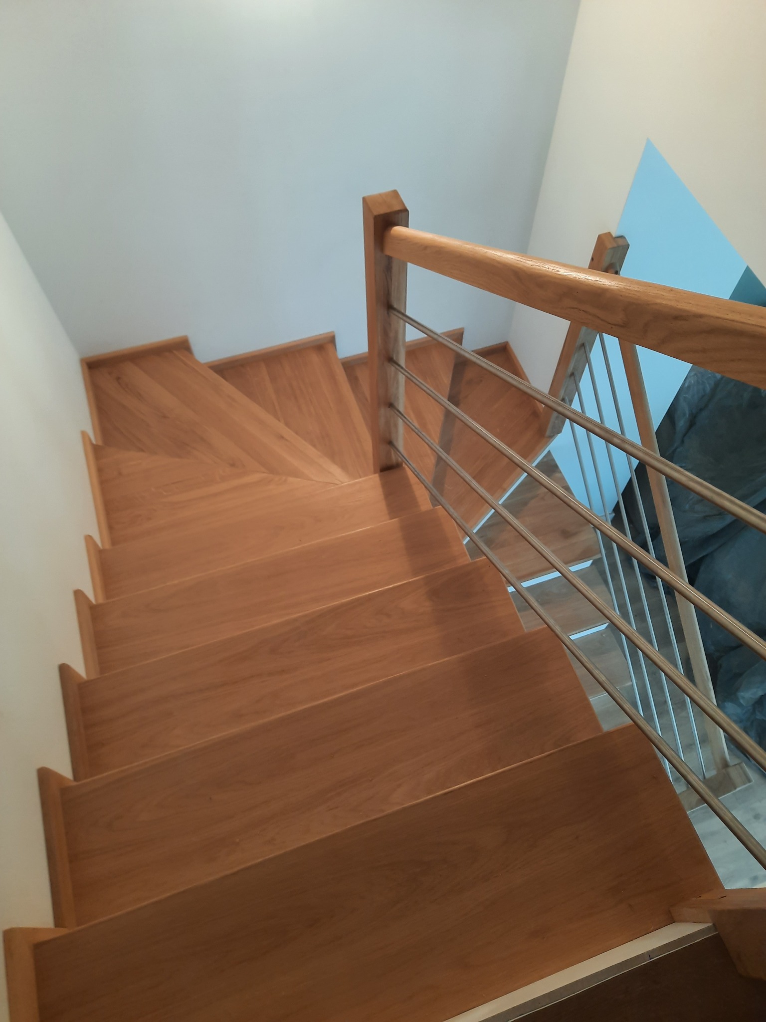 Drewniane schody z metalową balustradą widziane z góry. Naturalne oświetlenie podkreśla ciepły odcień drewna. Minimalistyczny design pasuje do nowoczesnego wnętrza.