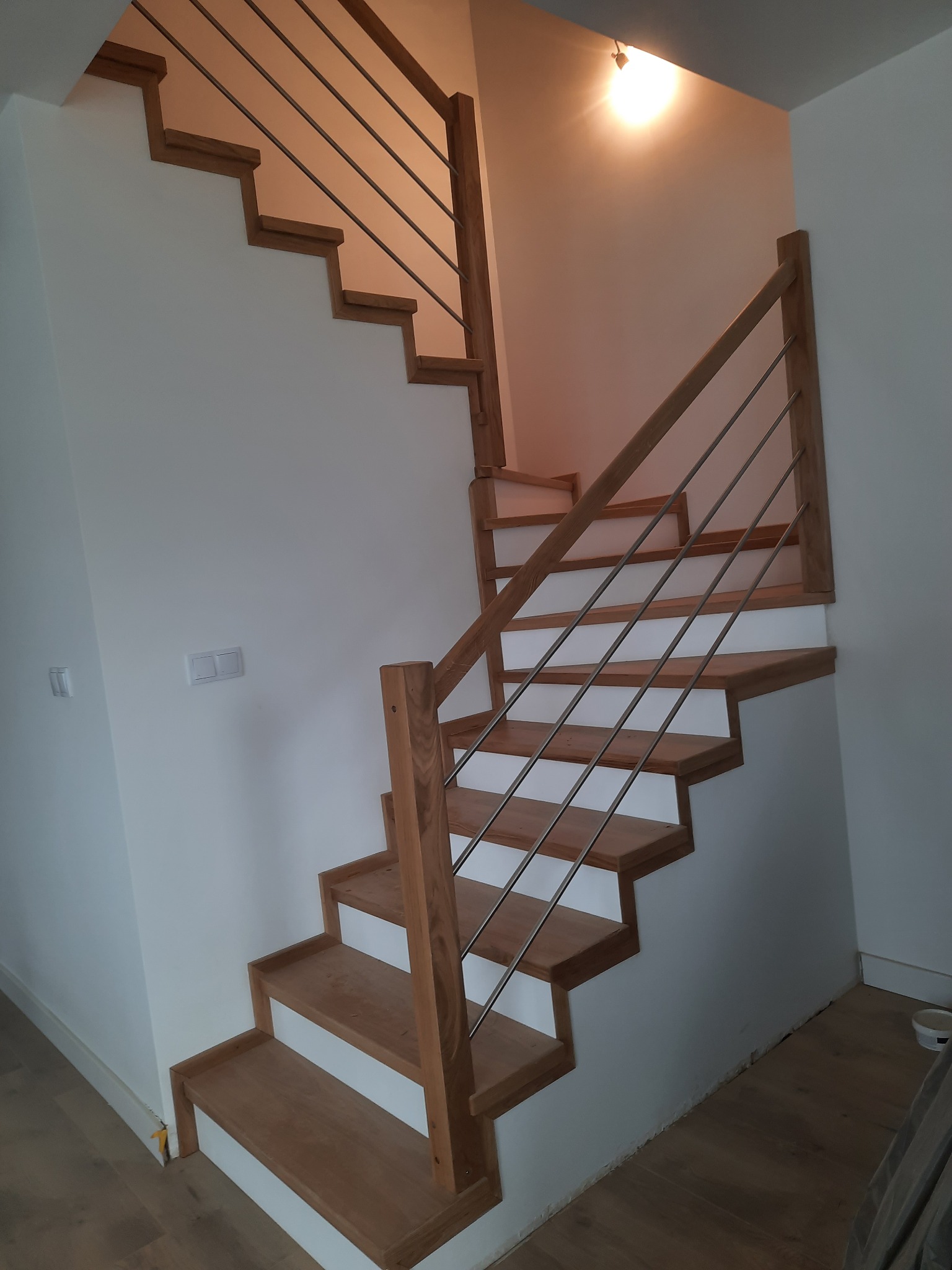 Nowoczesne, drewniane schody z metalowymi elementami w Olsztynie. Jasne drewno stopni kontrastuje z bielą ścian. Widoczne minimalistyczne wykończenie.