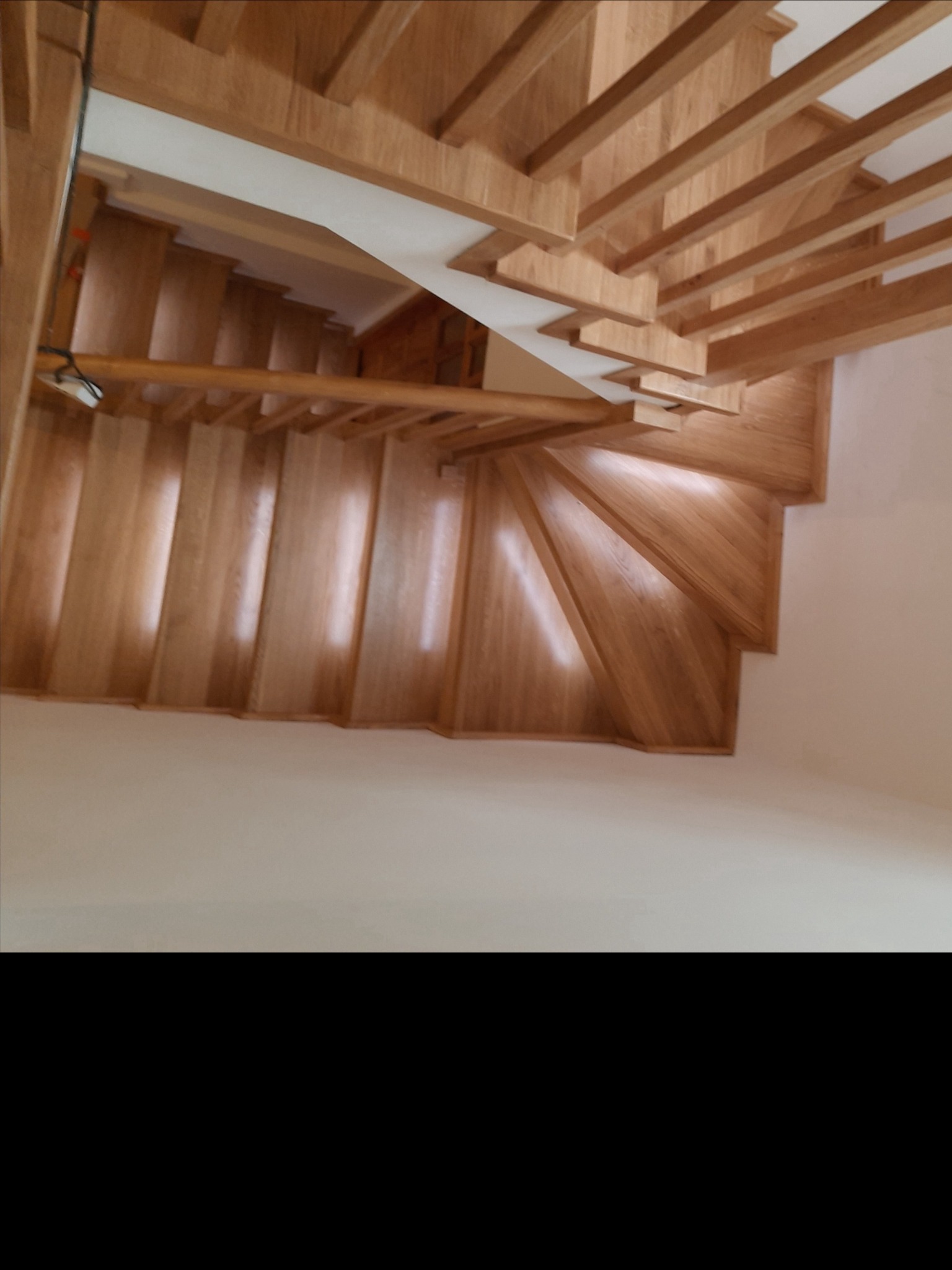 Jasne, dębowe schody z drewnianą poręczą, widok z góry. Stopnie skręcają, tworząc spiralny bieg. Naturalne światło podkreśla strukturę drewna.