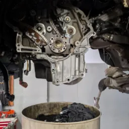 Olej silnikowy spływa do miski podczas naprawy silnika samochodowego w warsztacie. Widoczne narzędzia i elementy silnika.