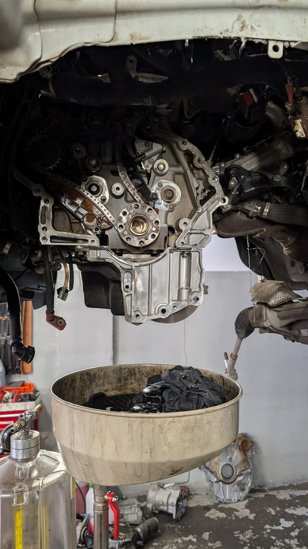 Olej silnikowy spływa do miski podczas naprawy silnika samochodowego w warsztacie. Widoczne narzędzia i elementy silnika.