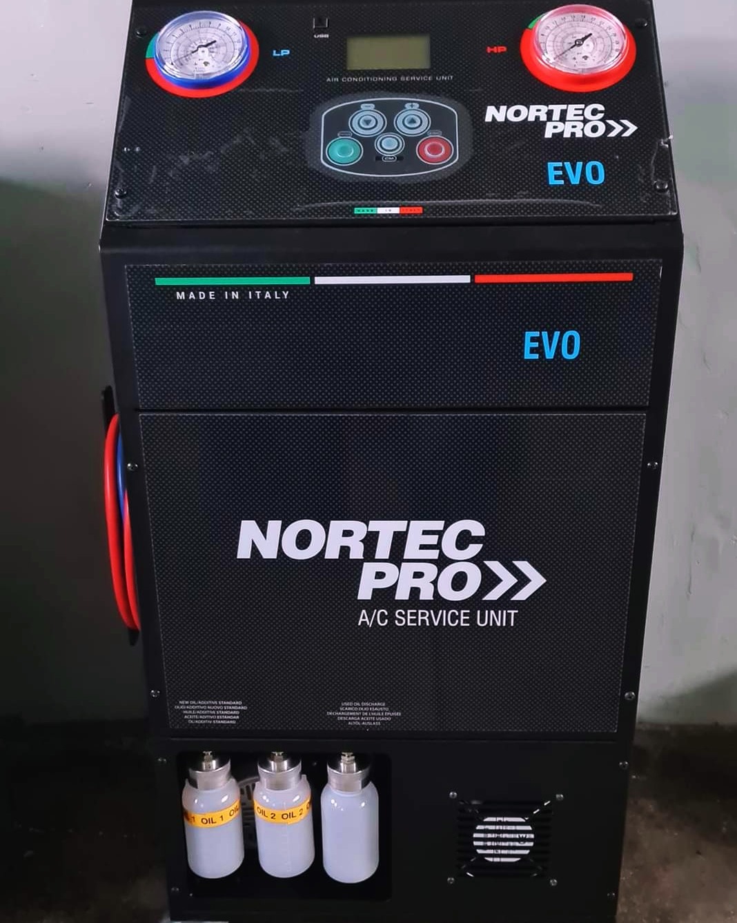 Profesjonalna stacja do obsługi klimatyzacji samochodowej Nortec Pro EVO z manometrami, wyświetlaczem i zbiornikami oleju. Sprzęt warsztatowy z napisem 'Made in Italy'.