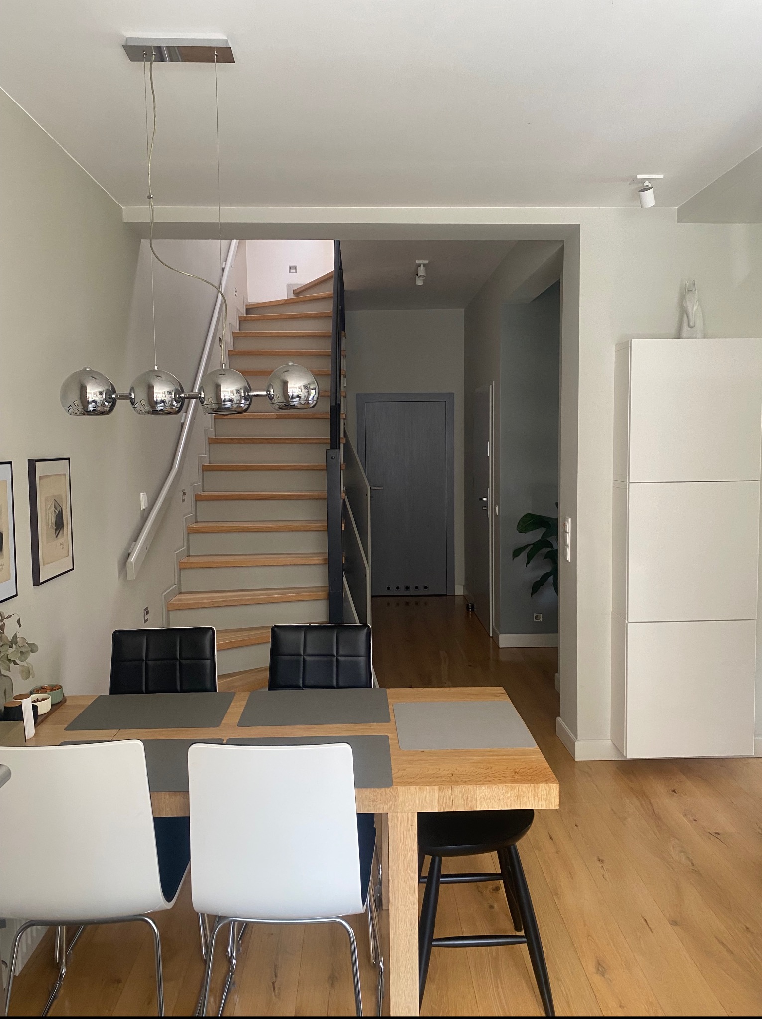 Jasna jadalnia z drewnianym stołem i schodami w tle, oświetlona lampą kulistą. Minimalistyczny wystrój wnętrza w mieszkaniu w Poznaniu.