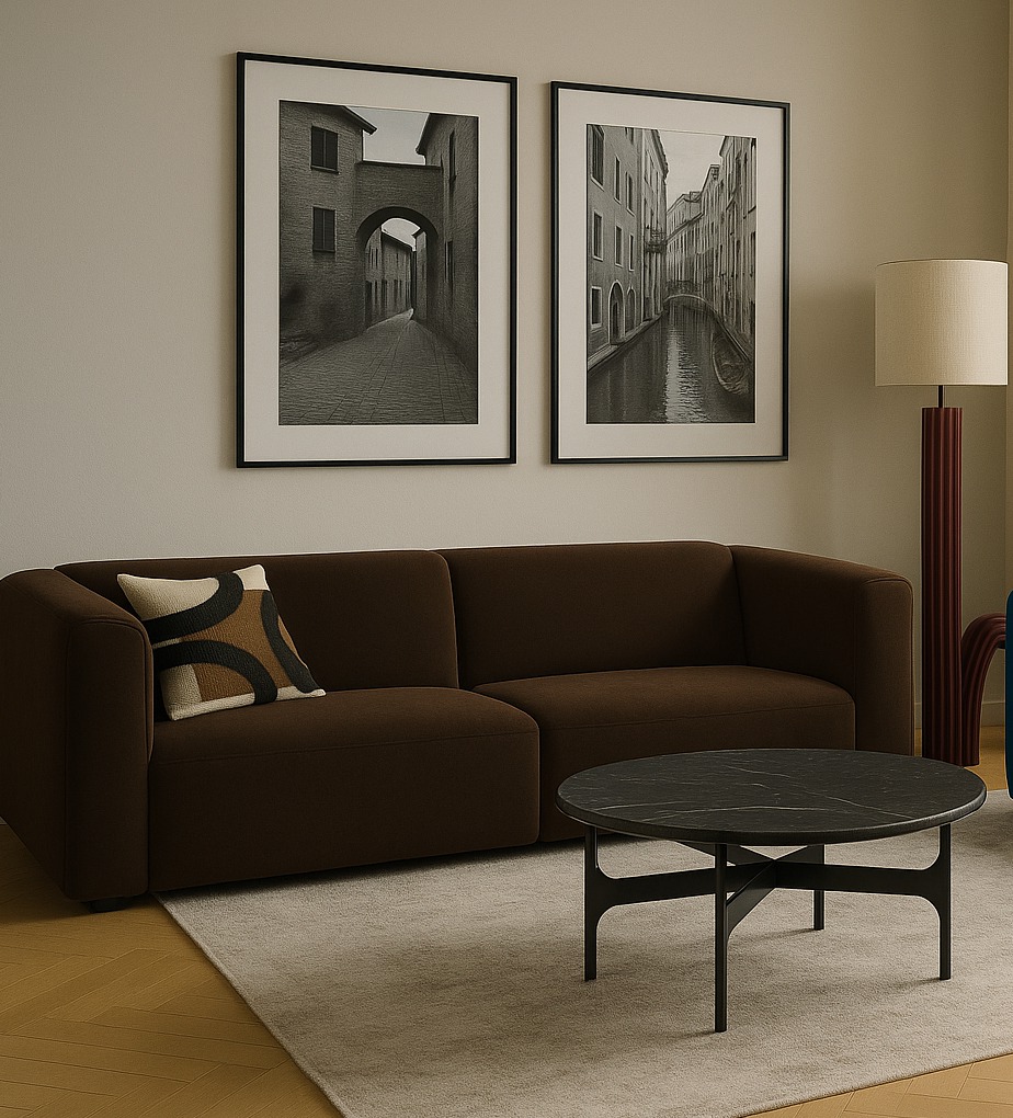 Nowoczesny salon z brązową sofą modułową, okrągłym stolikiem kawowym z czarnego marmuru i dwoma czarno-białymi fotografiami w czarnych ramach na ścianie.