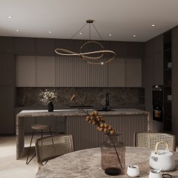 MadLine Studio - Stylowa kuchnia w odcieniach brązu z marmurowym blatem, oświetlona nowoczesną lampą. Na stole wazon z gałązkami i biały czajnik, dodające wnętrzu przytulności.