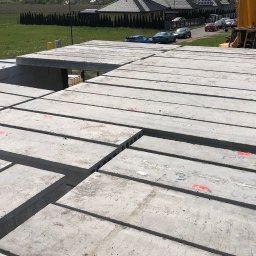 MM POLBUD Paweł Olbryś - Montaż prefabrykowanych płyt stropowych na budowie domu jednorodzinnego. Widoczny żuraw i elementy konstrukcyjne. Płyty z oznaczeniami. Ujęcie z góry.