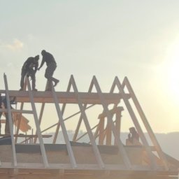 MM POLBUD Paweł Olbryś - Ekipa monterów w trakcie wznoszenia drewnianej konstrukcji dachu domu jednorodzinnego na tle zachodzącego słońca. Elementy konstrukcyjne z drewna.