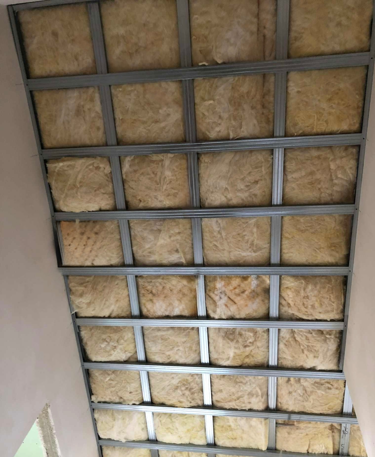 Skośny sufit poddasza z metalową konstrukcją i wypełnieniem z wełny mineralnej, widok z dołu, etap ocieplania.