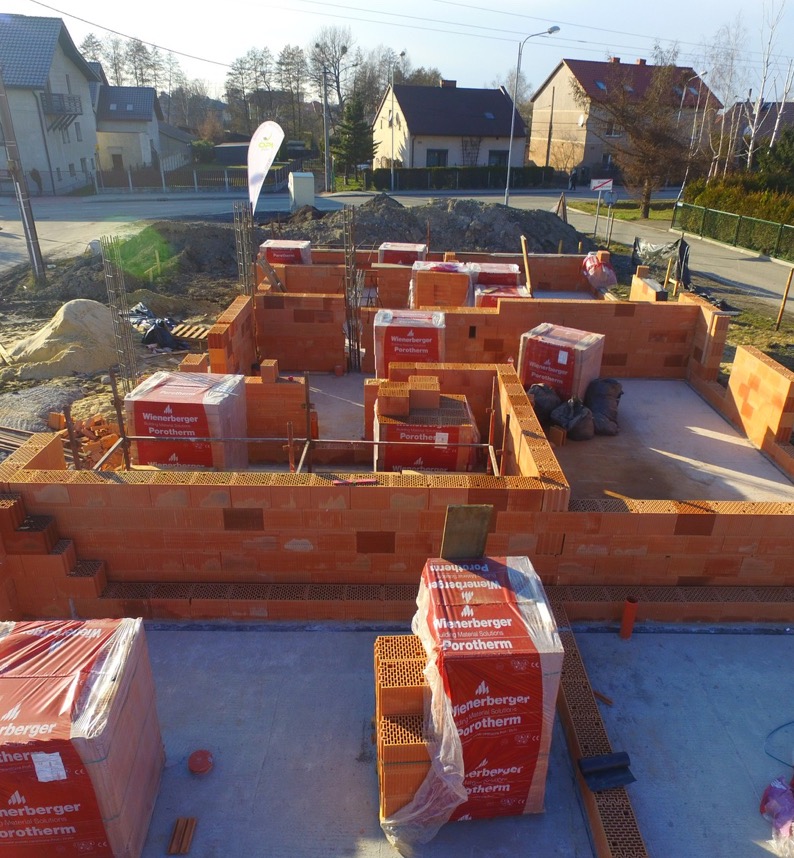Budowa domu z bloczków Porotherm: wzniesione ściany fundamentowe, palety z materiałem na placu budowy. Widok z góry na budowę w trakcie wznoszenia ścian.