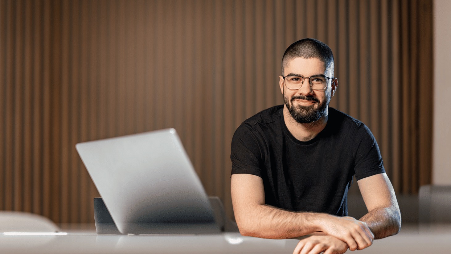 Uśmiechnięty copywriter z Oławy w okularach, siedzący przy biurku z laptopem. Profesjonalny wizerunek dla agencji interaktywnej.