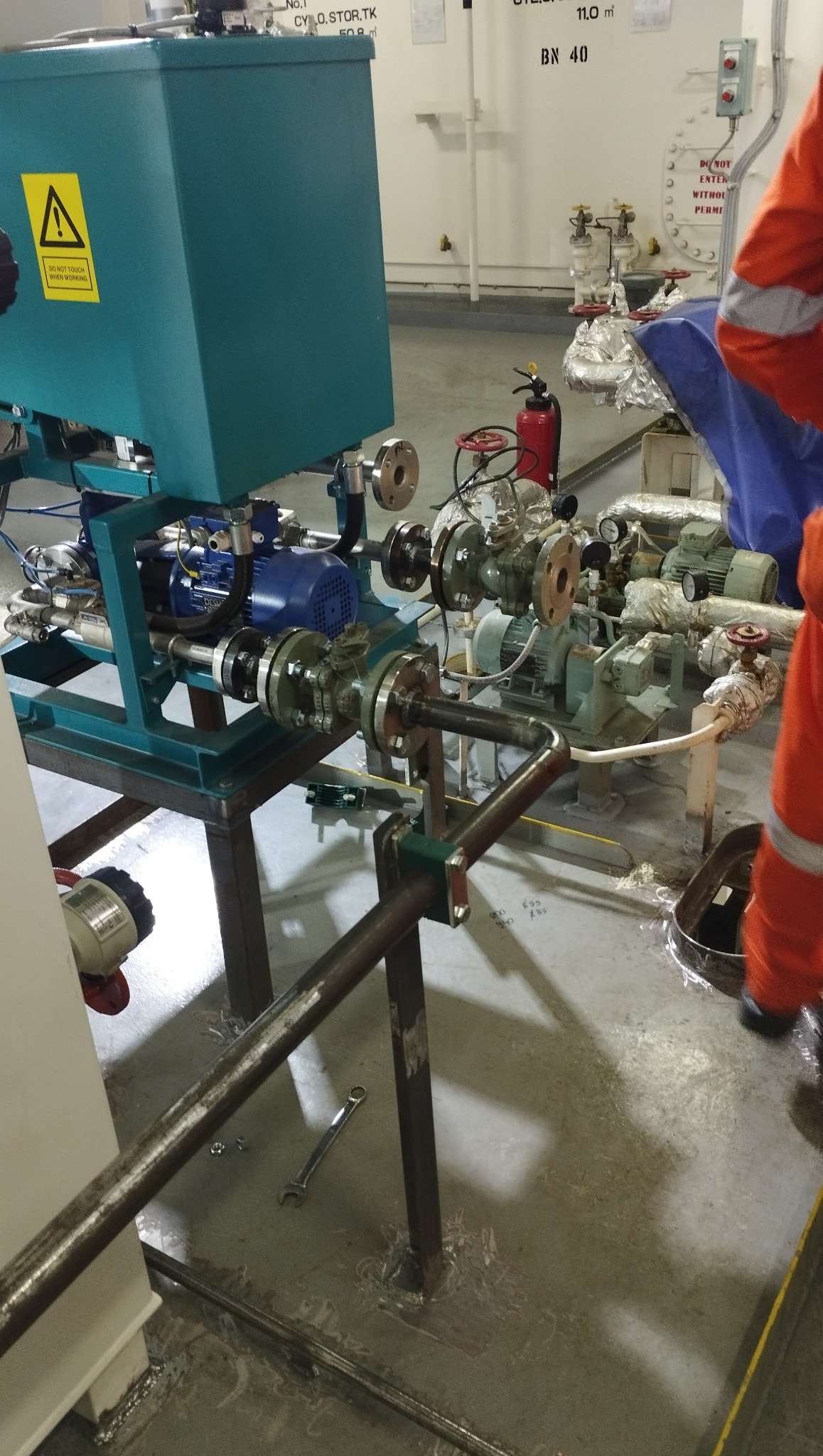 Konstrukcja z rur i metalowych elementów w hali, prawdopodobnie w trakcie montażu lub serwisu. Widoczny silnik, zawory, zbiornik i narzędzia.