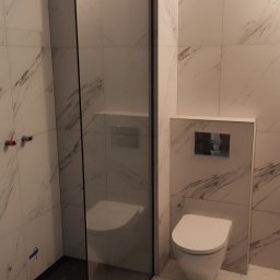Marcin Gut Merkosmik - Nowoczesna łazienka z kabiną prysznicową typu walk-in i podwieszaną toaletą. Białe płytki z marmurowym wzorem. Minimalistyczny design, czarne akcenty.