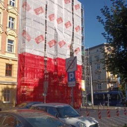 LDV - Budynek w rusztowaniach, osłonięty siatką z logo firmy KABE, częściowo w barwach flagi Polski. Prace wysokościowe w mieście.