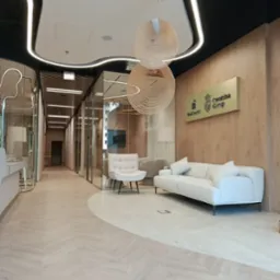 Eleganckie wnętrze biura z drewnianą okładziną, białymi meblami i designerskimi lampami. Parkiet ułożony we wzór jodełki, szklane ściany działowe.