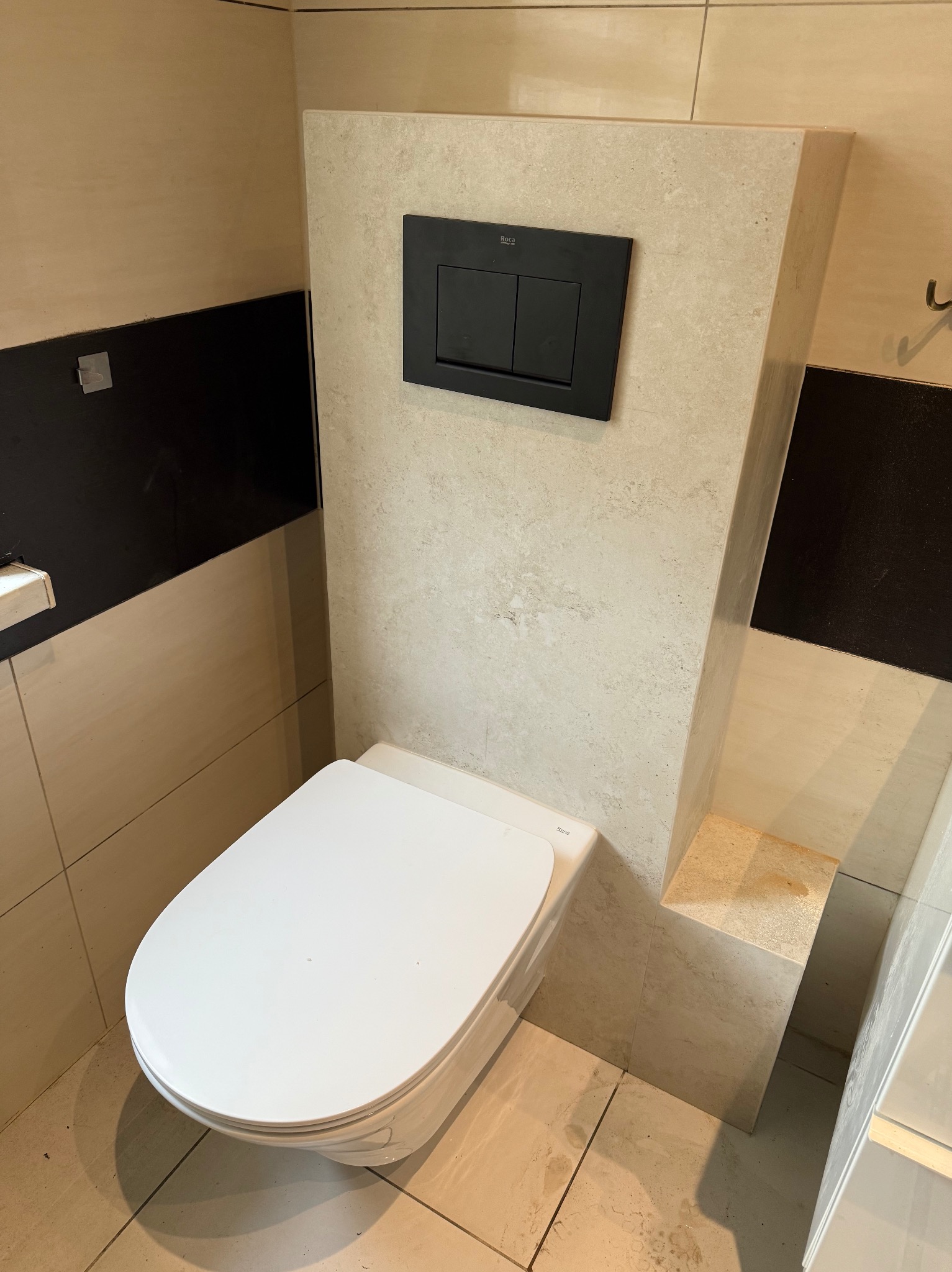 Podwieszana toaleta z czarnym panelem spłukującym na beżowej ścianie z płytek, element wykończenia łazienki w nowoczesnym stylu, widok z góry.