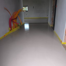 Usługi Ogolnobudowlane - Wnętrze w trakcie prac wykończeniowych: wylana posadzka samopoziomująca, zabezpieczona folią, widoczne kable instalacji elektrycznej przy ścianie.