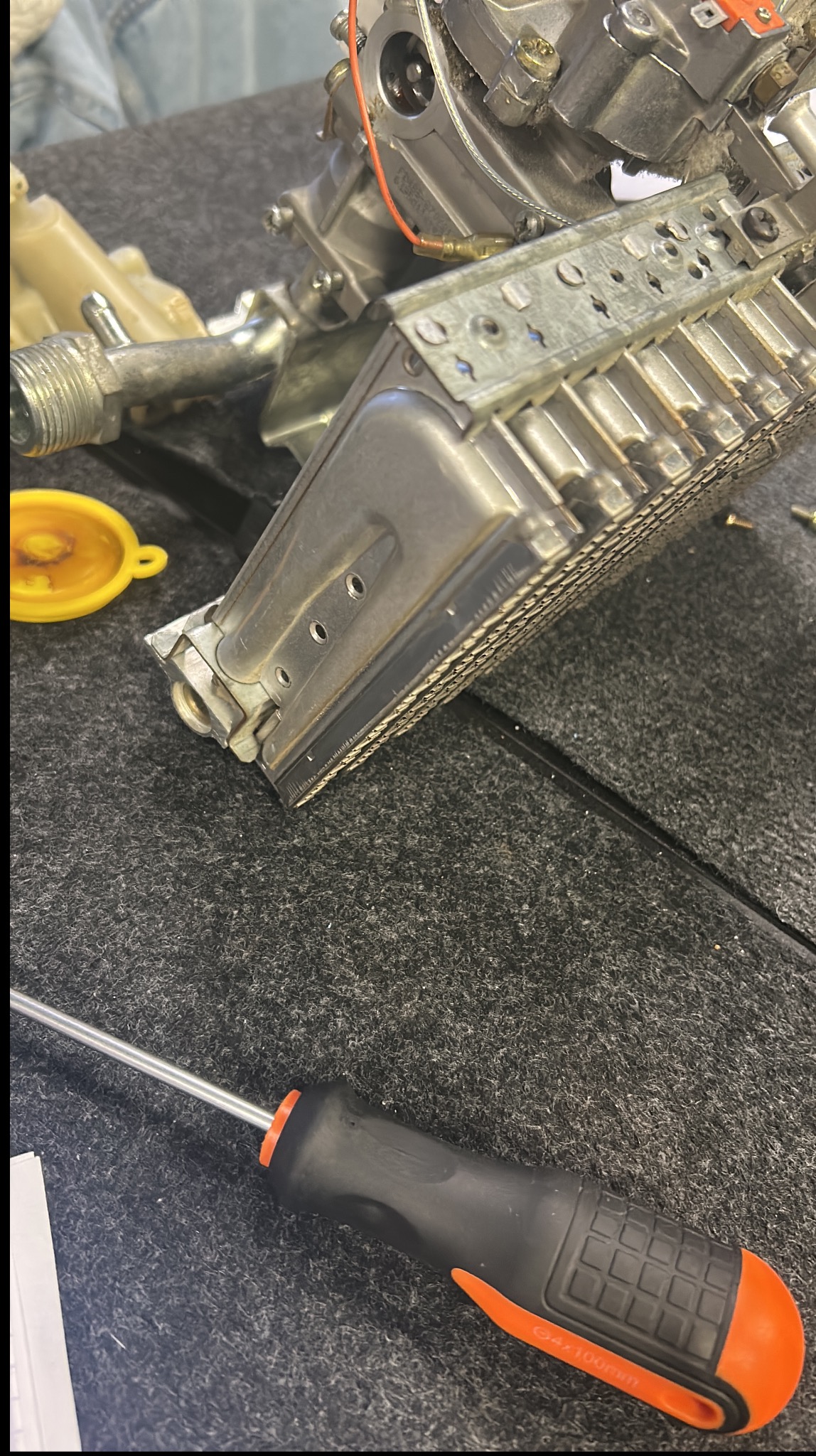 Detale pieca gazowego na szorstkiej powierzchni z widocznym śrubokrętem. Elementy metalowe, złącza, śruby, i pomarańczowy uchwyt narzędzia.