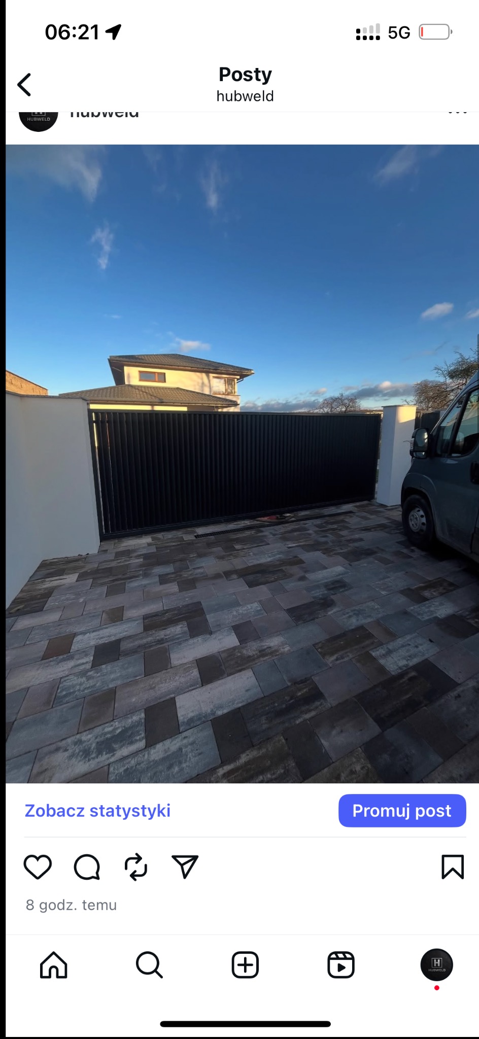 Nowoczesna, przesuwna brama wjazdowa z pionowych, czarnych profili, zamontowana na posesji z kostką brukową. W tle widoczny dom z szarą dachówką.