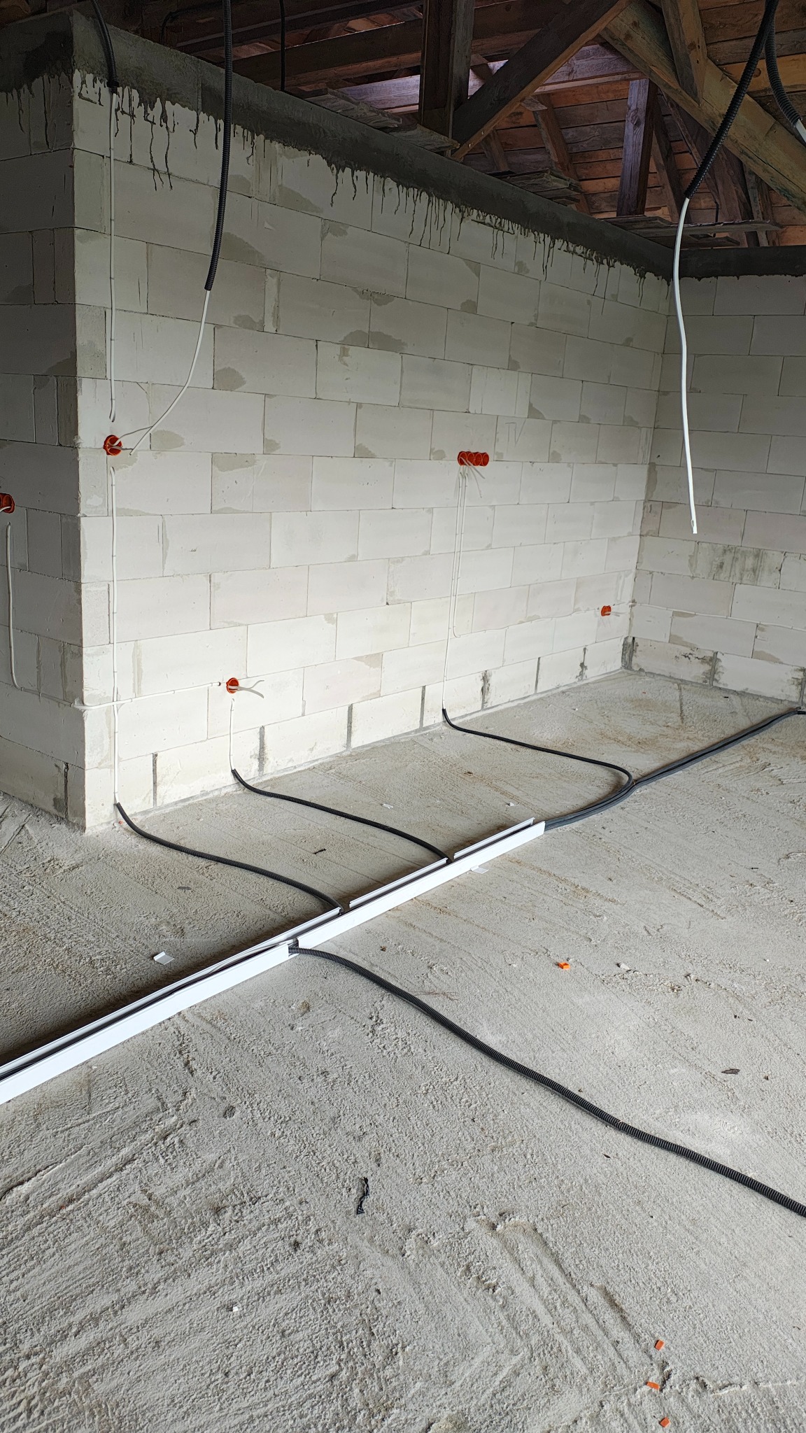 Wnętrze w trakcie prac elektrycznych: kable w peszlach ułożone na podłodze, przewody wyprowadzone ze ścian z pustaków, widoczne puszki instalacyjne.