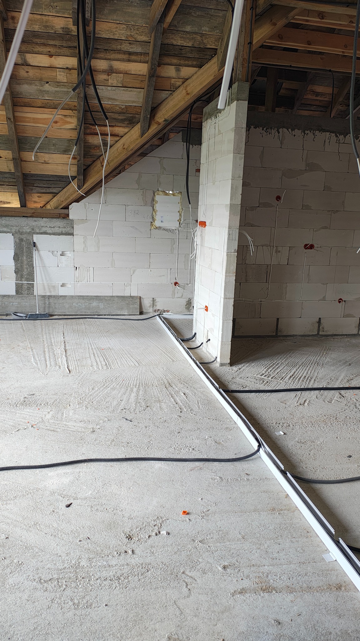 Wnętrze w trakcie prac: kable elektryczne w peszlach ułożone na podłodze, puszki elektryczne w ścianach z białego bloczka, drewniana więźba dachowa.
