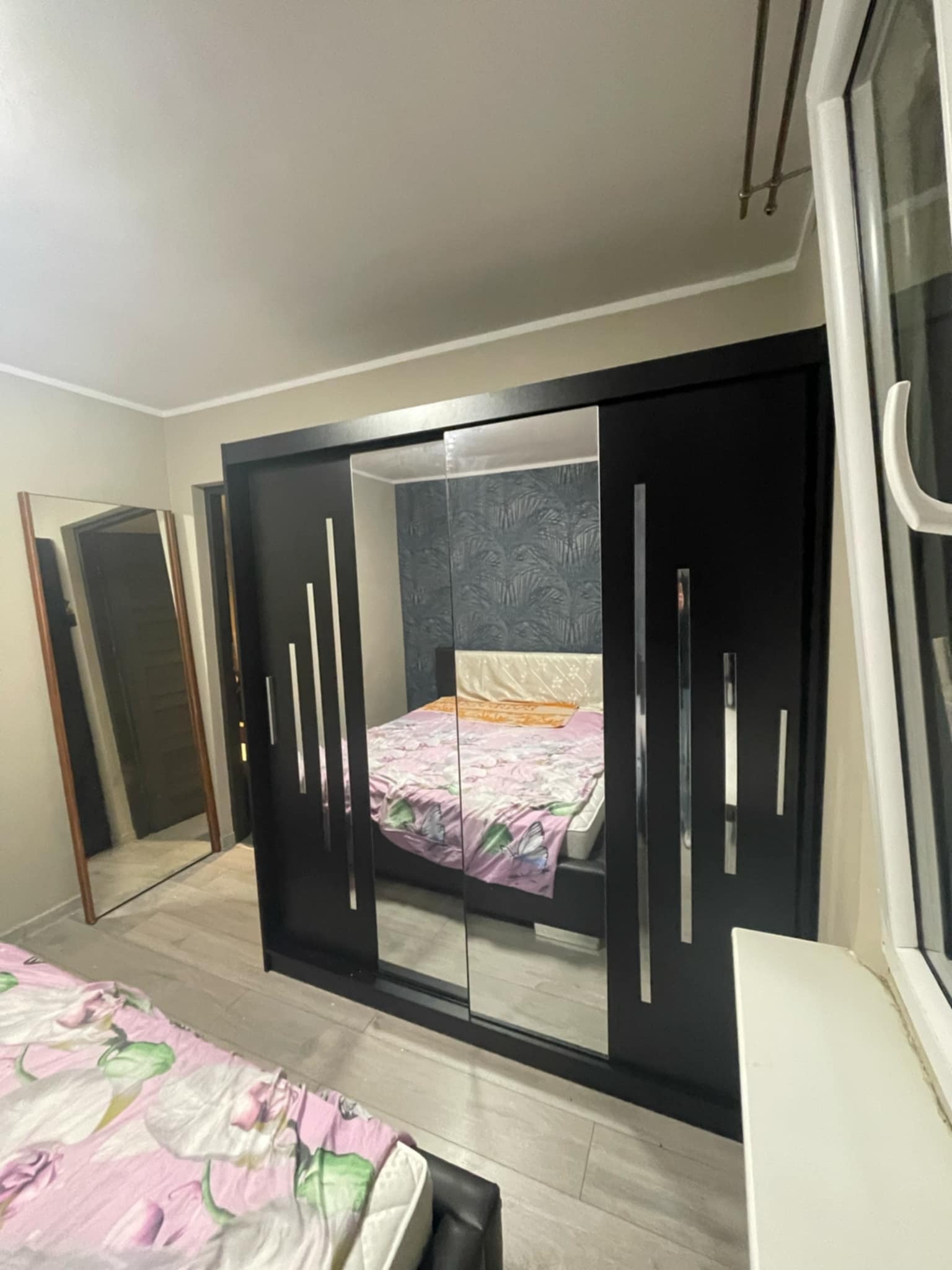 Czarna szafa przesuwna z lustrami w sypialni w Tychach. Widoczne odbicie łóżka i tapety. Minimalistyczny design z chromowanymi akcentami.