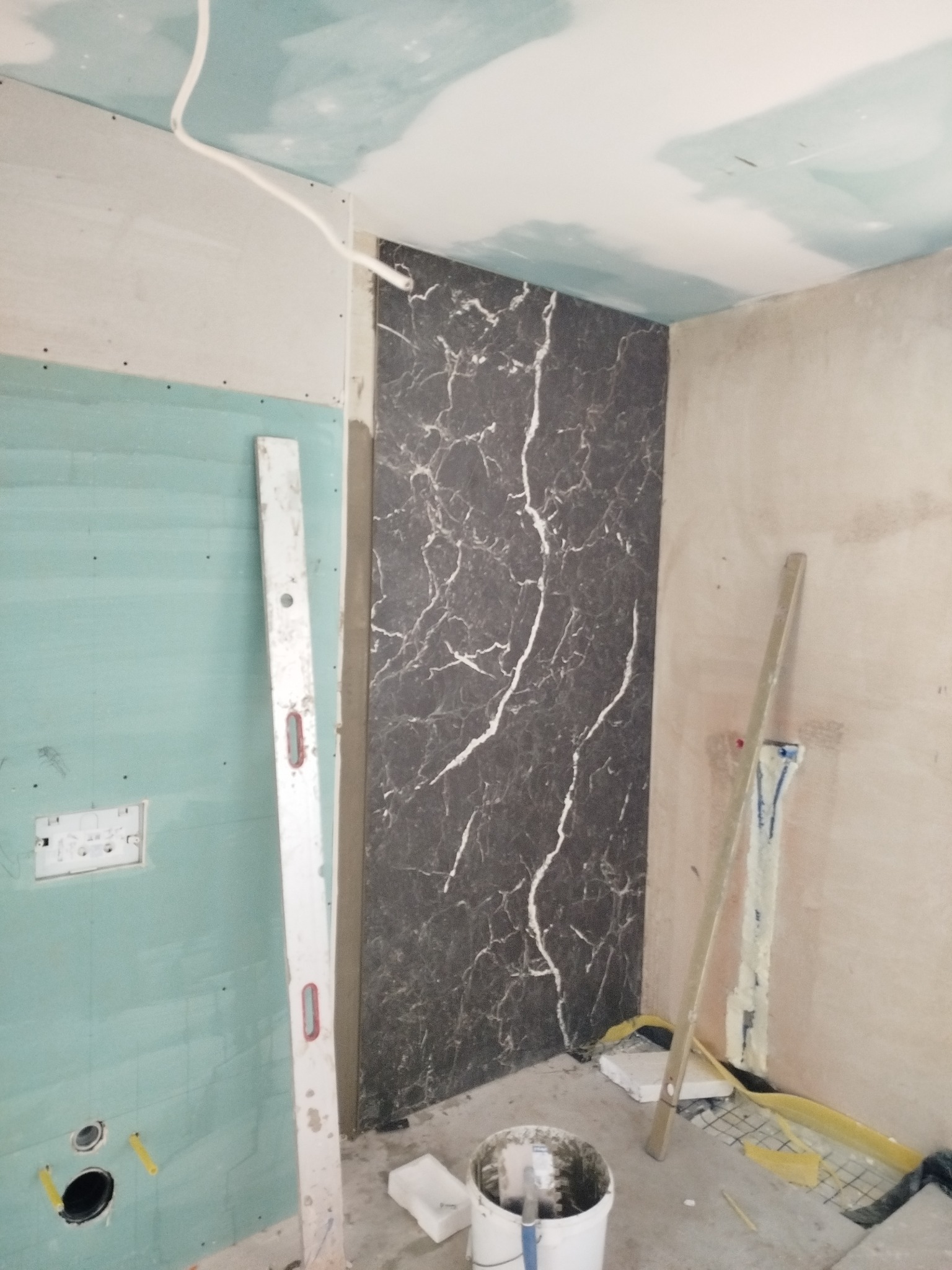 Montaż płytek imitujących marmur na ścianie w łazience w trakcie remontu. Widoczne narzędzia, poziomica i płyta karton gips na ścianach.