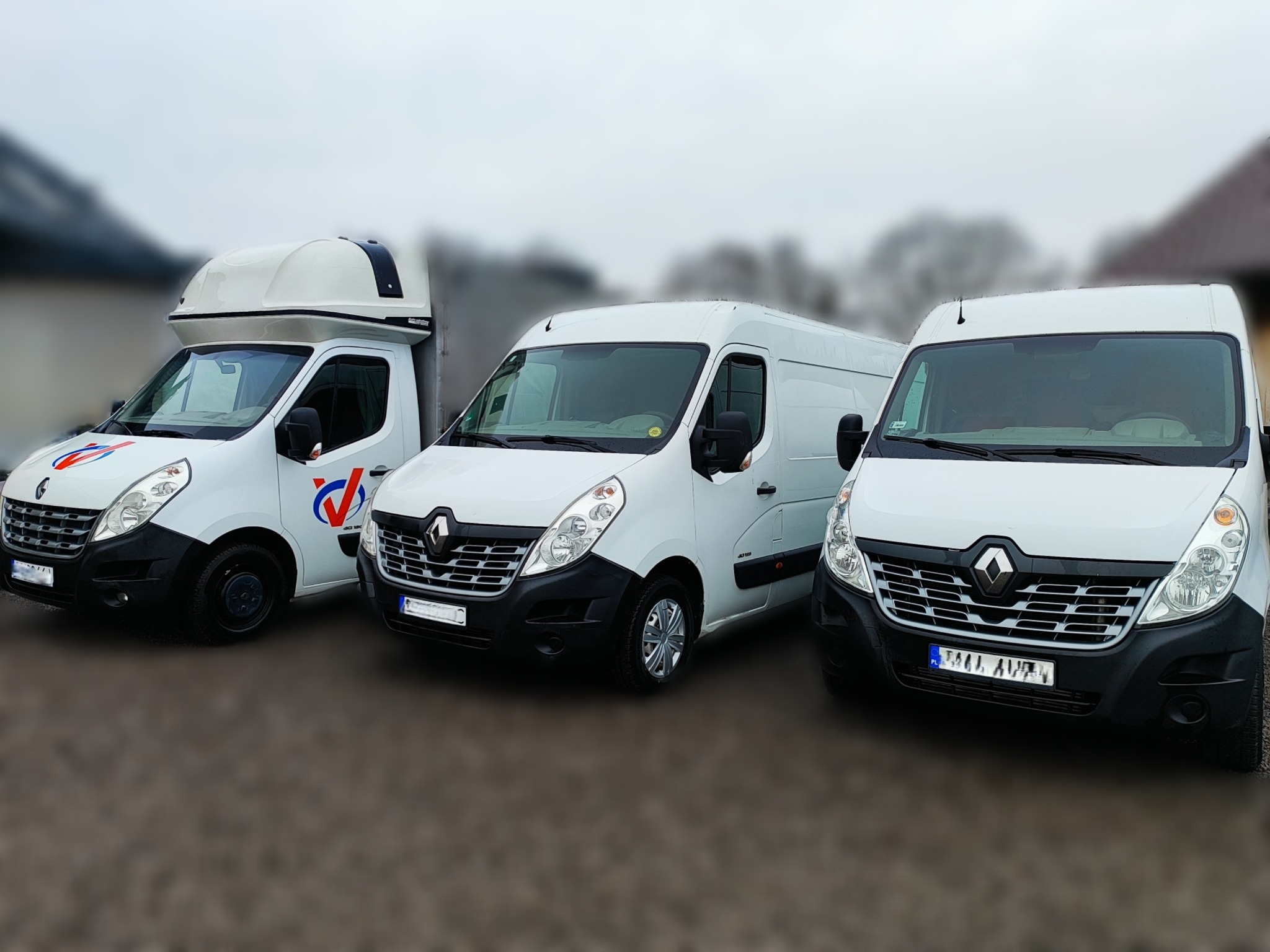 Trzy białe busy Renault Master zaparkowane obok siebie. Jeden z zabudową kontenerową, drugi furgon, trzeci z podwyższonym dachem. Szare niebo, budynek w tle.