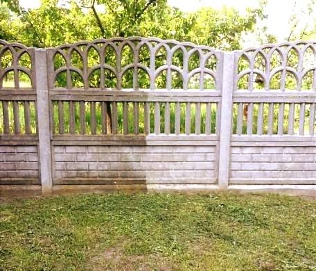 Czyszczenie betonowego ogrodzenia: połowa wyczyszczona, połowa zabrudzona, ukazująca efekt mycia ciśnieniowego. Widoczne trawa i drzewa w tle.