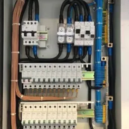 Rozdzielnica elektryczna: precyzyjnie ułożone kable w kolorach miedzi i niebieskim, zabezpieczenia, szyny DIN w skrzynce. Instalacja elektryczna wewnątrz.