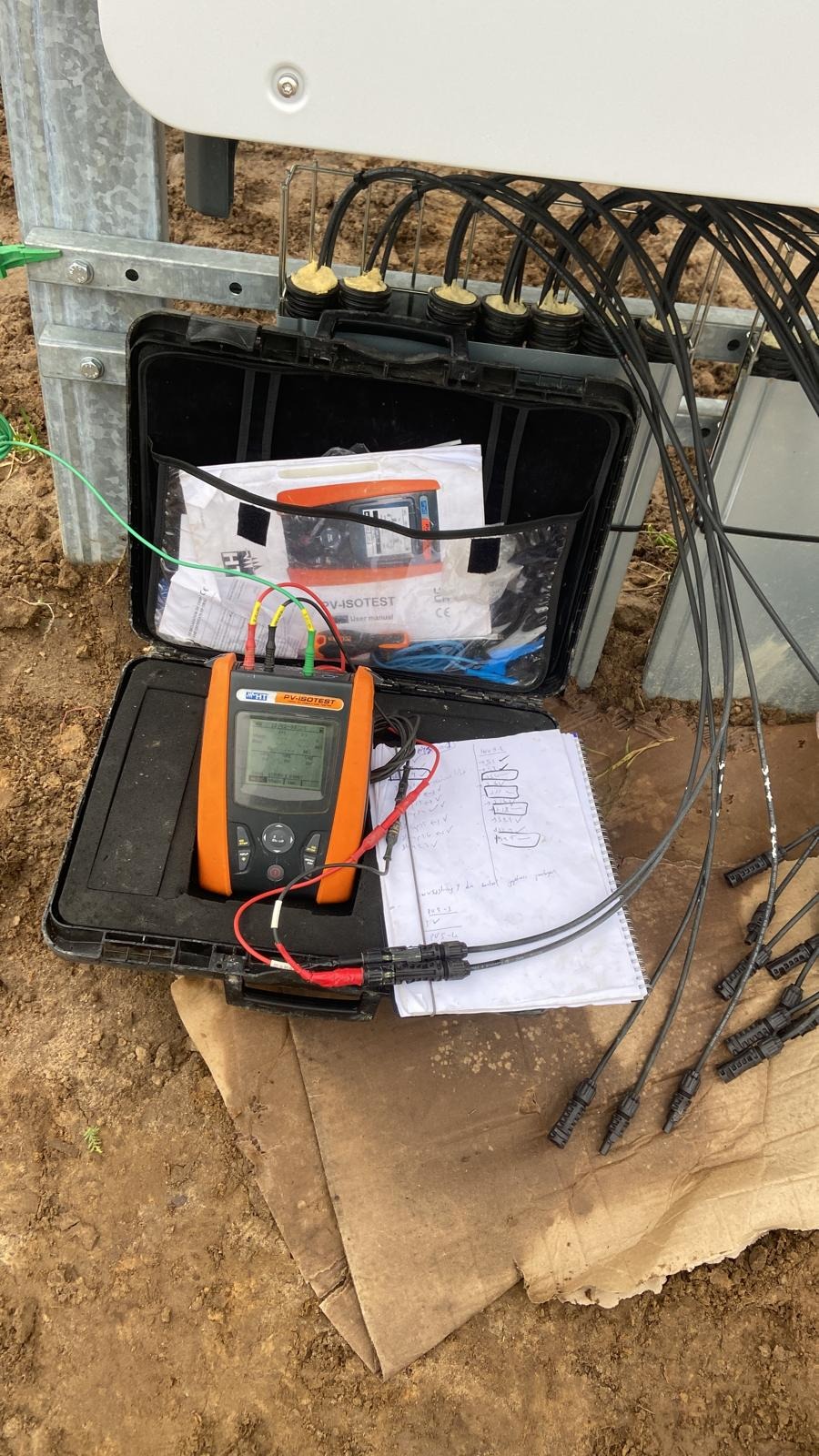 Pomiar instalacji fotowoltaicznej: otwarty kufer z miernikiem PV-ISOTEST, notatnik z pomiarami, przewody i złącza. Kontrola jakości i bezpieczeństwa.