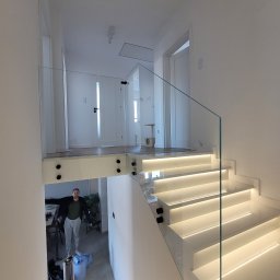 Z-Glass - Nowoczesna balustrada szklana na schodach z podświetleniem LED. Widoczna osoba w tle i minimalistyczny design wnętrza.