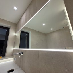 Z-Glass - Nowoczesna łazienka z podświetlanym lustrem i armaturą. Widoczne okno i elementy wykończenia w stonowanej kolorystyce. Minimalistyczny design z dbałością o detale.