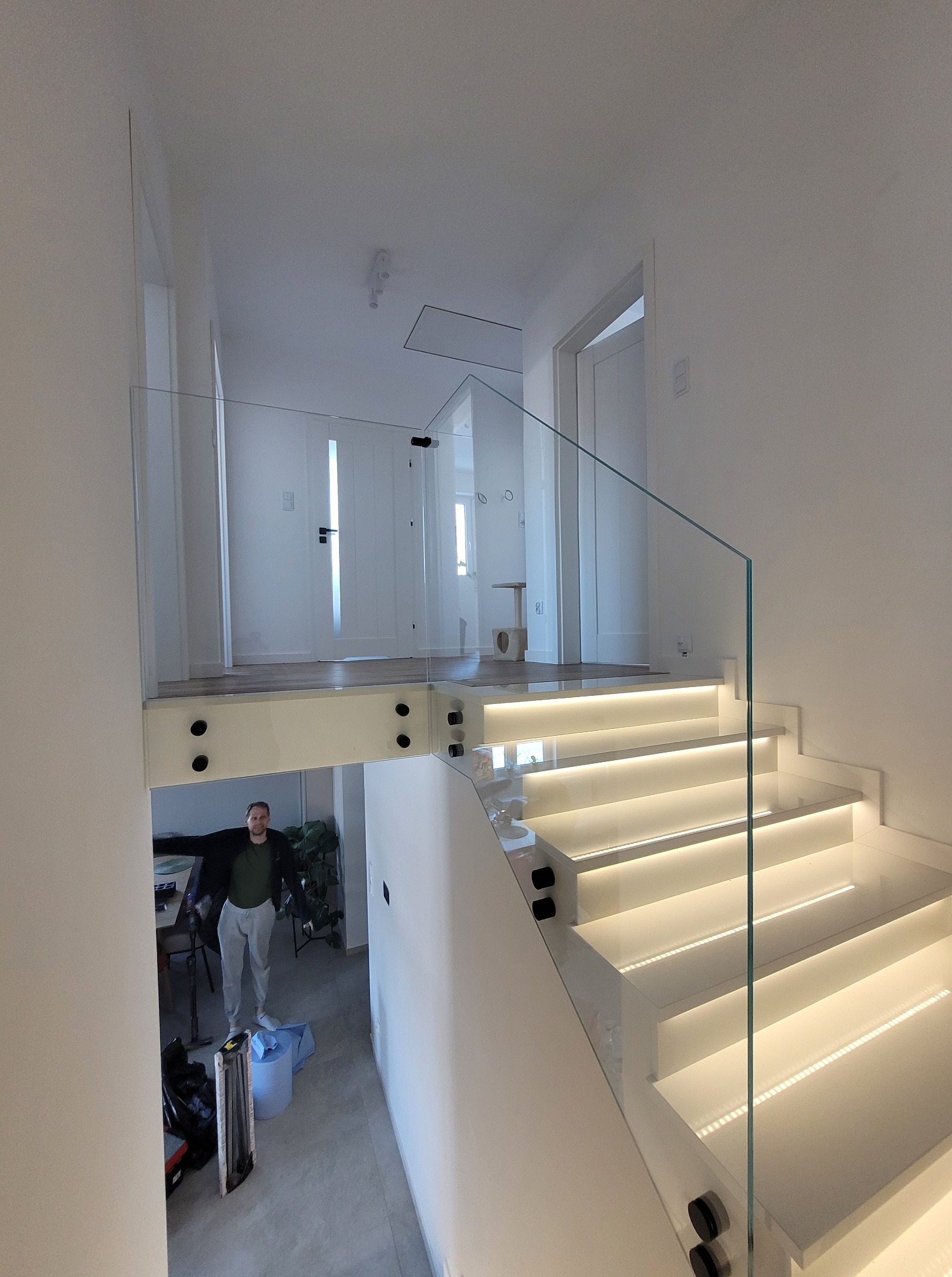 Nowoczesna balustrada szklana na schodach z podświetleniem LED. Widoczna osoba w tle i minimalistyczny design wnętrza.