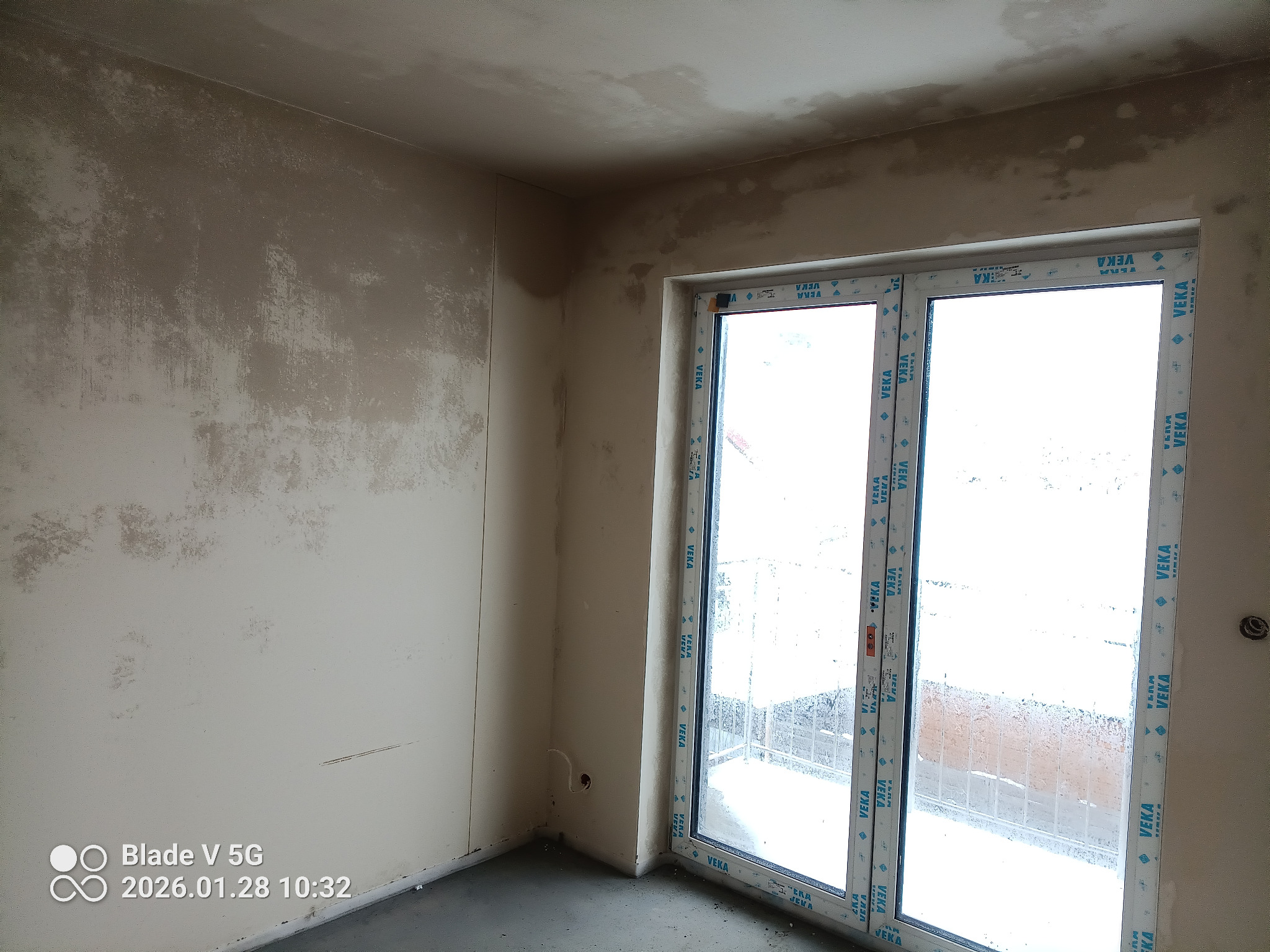 Pokój w trakcie prac tynkarskich: ściany pokryte warstwą tynku, widoczne okno balkonowe z ramą VEKA. Surowy stan wykończenia wnętrza.