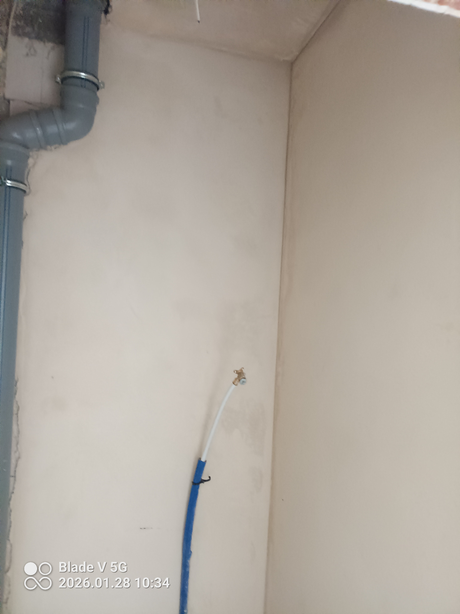 Ściana po tynkowaniu maszynowym z widoczną instalacją hydrauliczną i rurą kanalizacyjną. Jasne, neutralne tło. Widoczne detale instalacji.