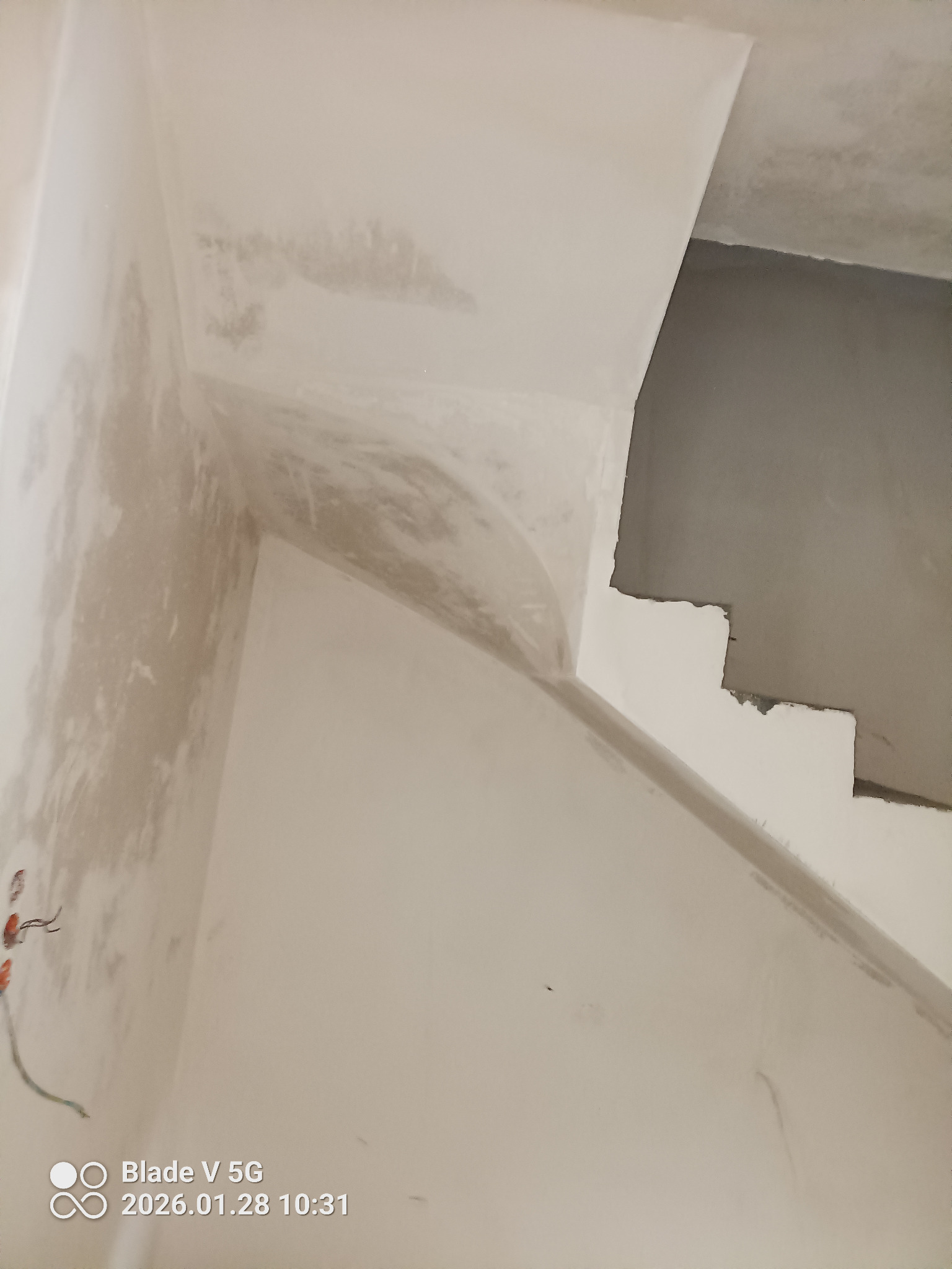 Ściana po nałożeniu gładzi gipsowej, widoczne fragmenty instalacji elektrycznej. Częściowo wykończone schody w surowym stanie. Ujęcie z dołu, blisko ściany.