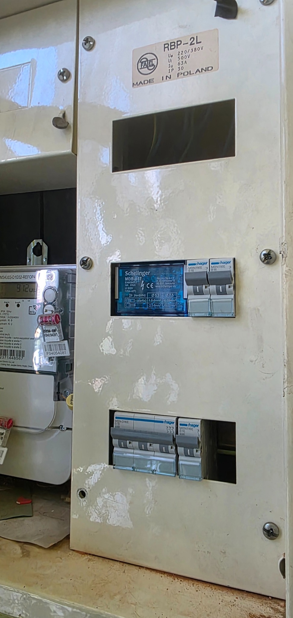 Rozdzielnica elektryczna z zamontowanymi bezpiecznikami Hager i licznikiem energii elektrycznej, widoczne oznaczenia producenta i parametry techniczne.